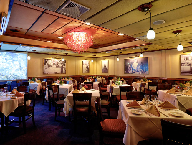 Photo of the private dining room with empty tables set with white table cloths and orange linen napkins. A striking Venetian glass chandelier is visible